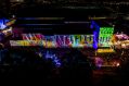 Boorloo Contemporary at East Perth Power Station (seen here in 2025) returns for Perth Festival 2026. An industrial-looking building lit up by brightly coloured projects, and photographed from the air at night; a large crowd is gathered in the building's expansive courtyard.