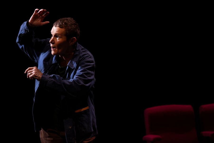 Genevieve Morris as Cory Taylor in the 2025 MTC production, 'Dying: A Memoir'. An older woman with short, greying hair poses dramatically on stage, as if shocked and automatically defending herself, perhaps by a sudden thunderclap.