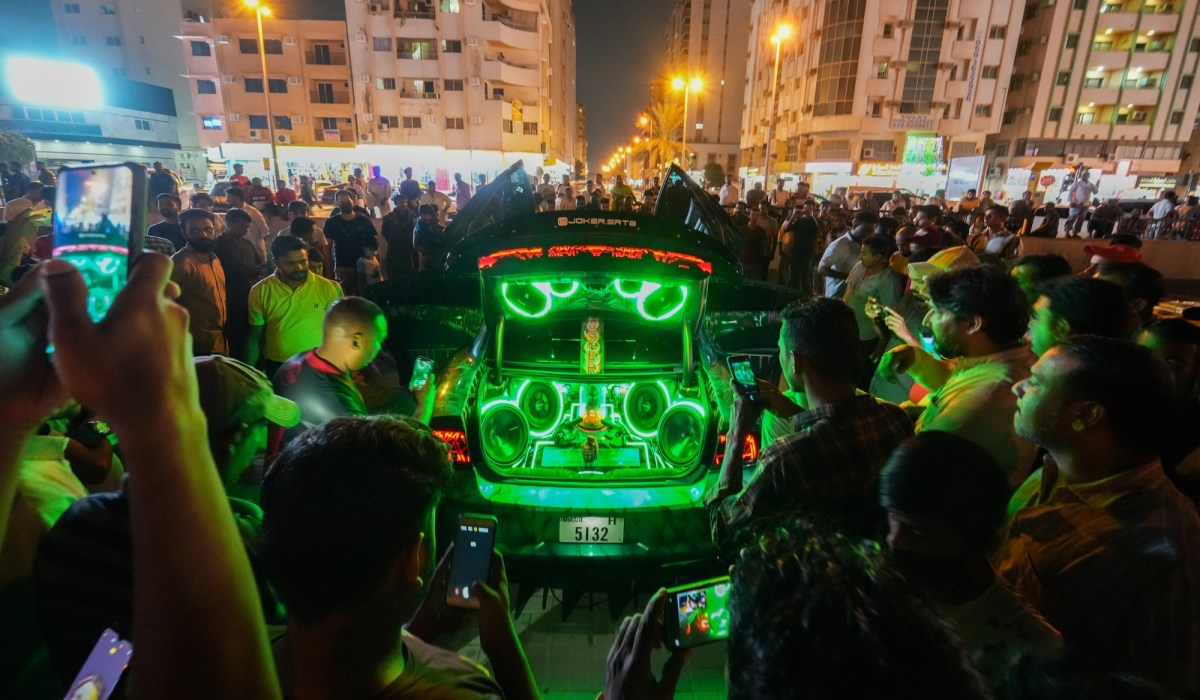 Crowd gathered around a car as art installation with green lights and music. Joe Namy