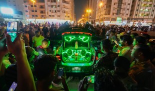 Crowd gathered around a car as art installation with green lights and music. Joe Namy
