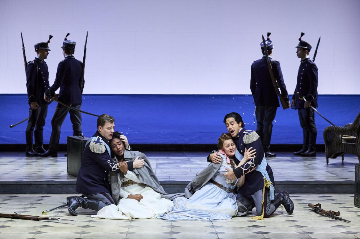 opera audiences: A theatre stage with four soldiers in shadow standing in pairs in the background. In the foreground are two soldiers, crouching on the ground, each one holding a woman in his arms. The women are wearing white gowns.