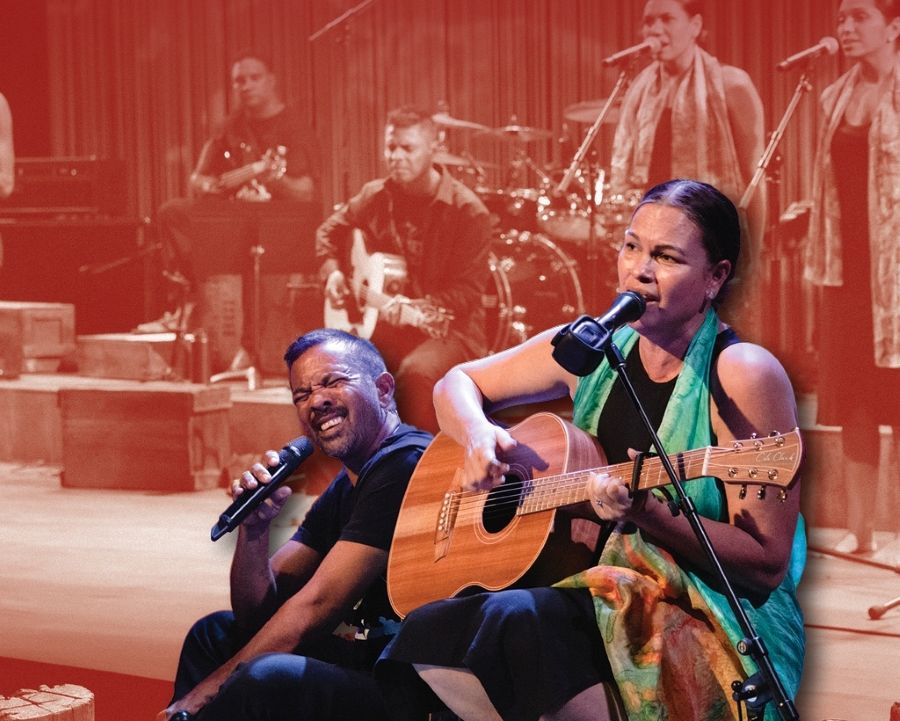 A promotional image for Black Swan State Theatre Company's 'Raised in Big Spirit Country', which plays Broome as part of the company's 2026 season. Two Aboriginal musicians, a seated man dressed in black and a colourfully dressed woman playing an accoustic guitar, sing on stage. Their images are overlaid on a sepia-toned image showing four other Aboriginal musicians and singers photographed mid-performance.