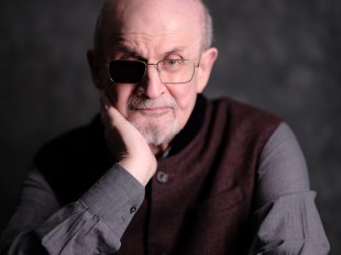 elderly man dressed in dark colors looking serious with one eye patch. Salman Rushdie