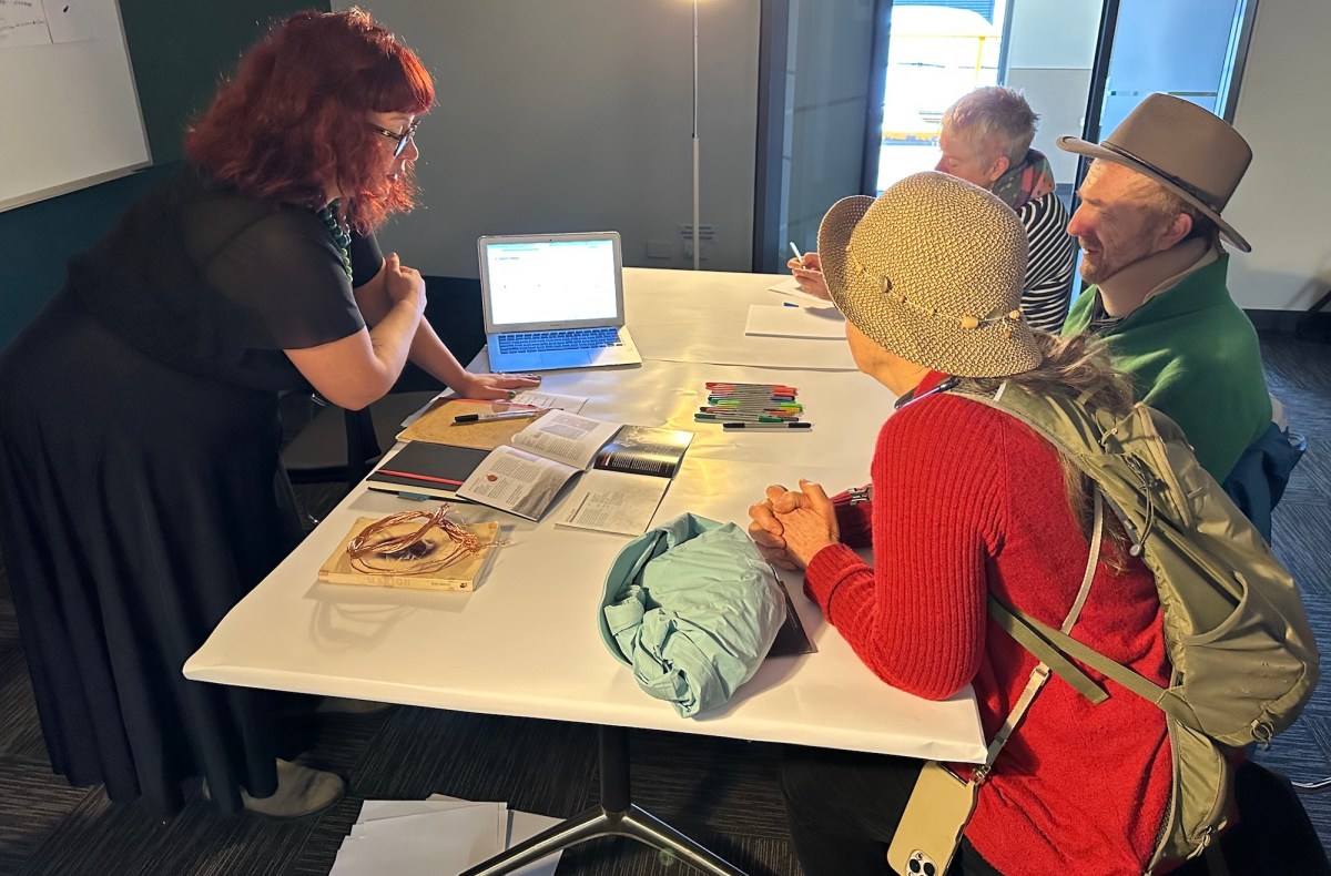 Woman at table with others talking about art in hands-on project. The Unconformity