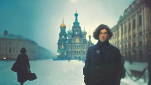 Publicity image for West Australian Opera's 2026 production 'Eugene Onegin'. A fair skinned man with thick black hair and wearing dark clothes stands in a snow-covered landscape; the domes and spires of a Russian Orthodox church are visible behind him.