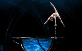 An acrobat balancing with one hand at the edge of a large goblet filled with water. Basic income Ireland.