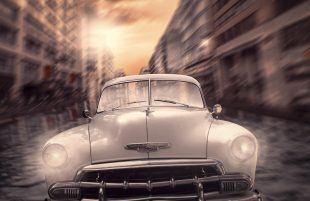 A 1950s-style car careers down a blurred street at speed, headlights blazing, towards the viewer. The image illustrates ArtsHub's weekly round-up of Australian arts sector appointments, On the move.
