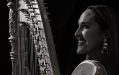 A black and white photo with high contract is a woman with her side profile holding a harp.