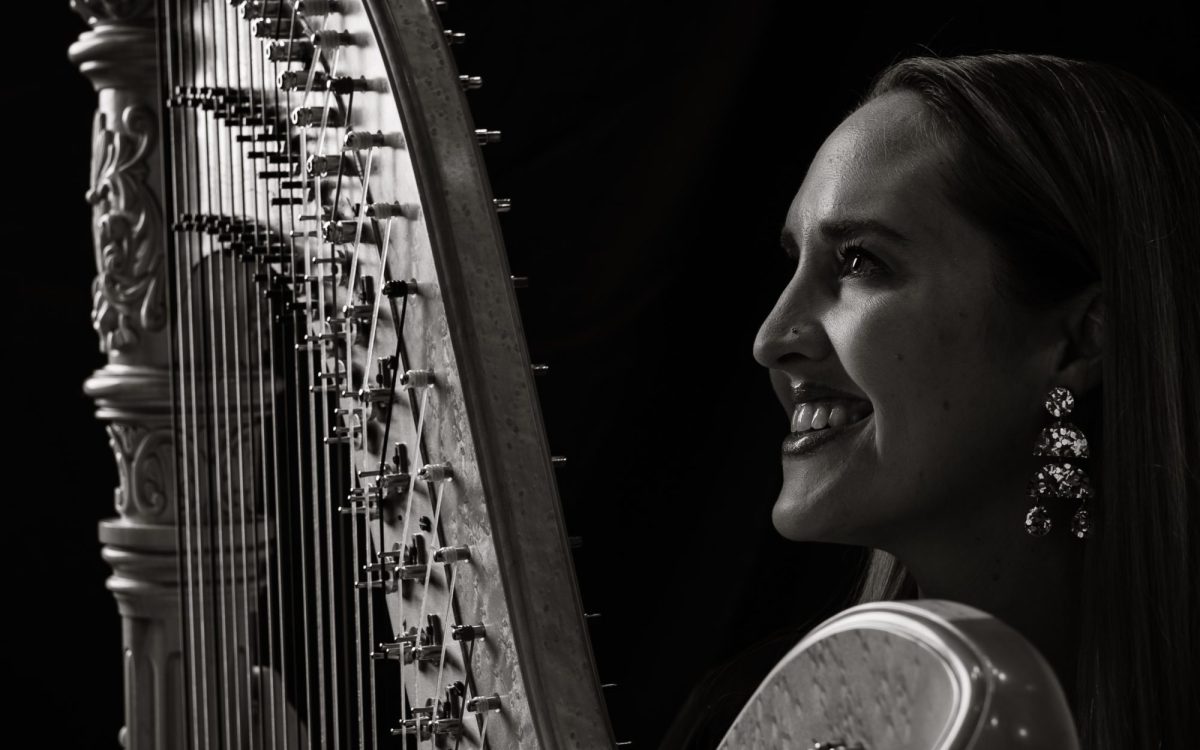 A black and white photo with high contract is a woman with her side profile holding a harp.