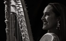 A black and white photo with high contract is a woman with her side profile holding a harp.