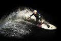 A photograph of a female surfer wearing in a black wetsuit and riding a wave; white spray flies up behind her board. The photo illustrates ArtsHub's weekly on the Move column of Australian arts sector appointments.