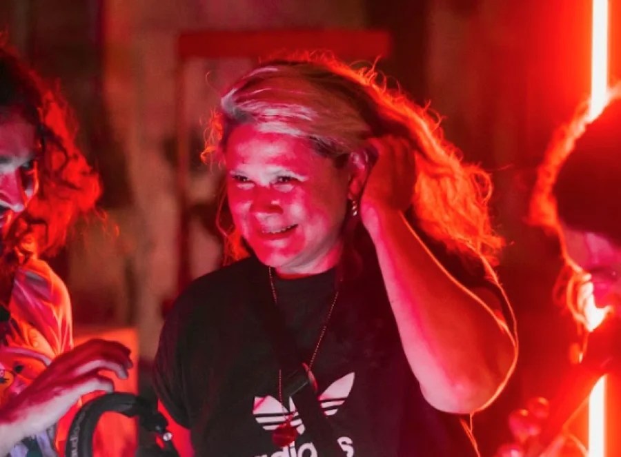 Liquid Architecture's outgoing CEO and Director Kristi Monfries. A fair-skinned woman in a black Adidas t-shirt smiles and pushes her dyed blonde hair behind her left ear.