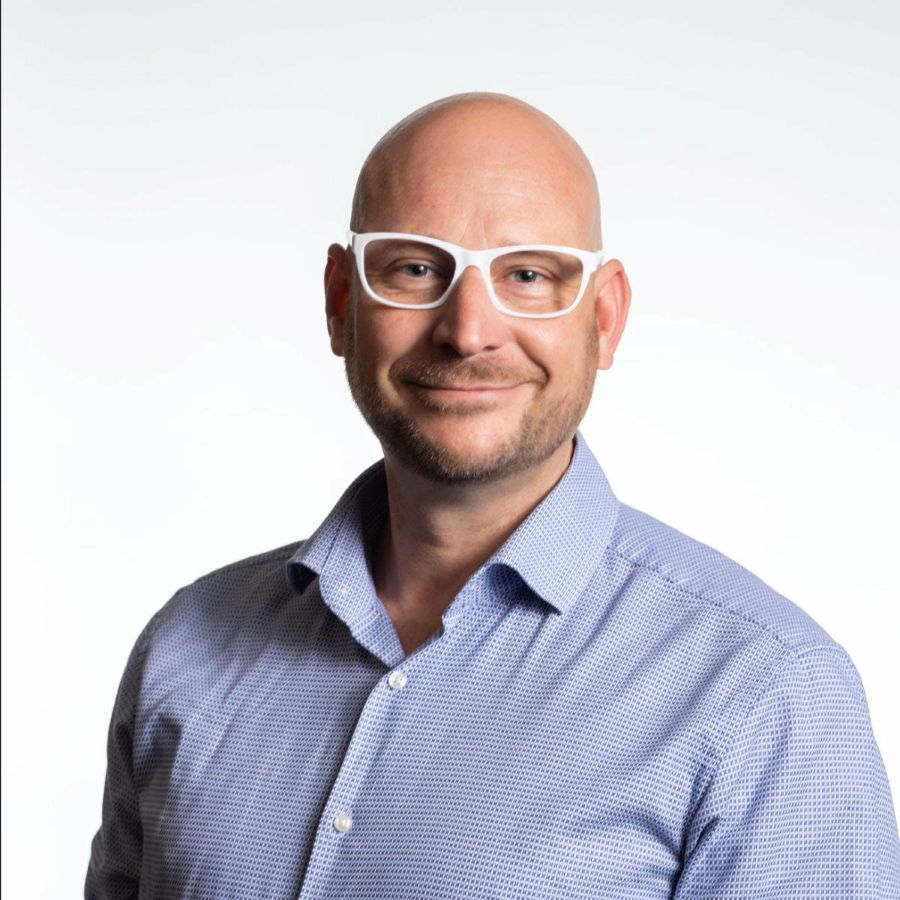 Rod Gilbert is The National’s new Chief Executive Officer. A fair-skinned man with a shaved head and white-rimmed glasses, and wearing a blue business shirt, smiles at the camera.