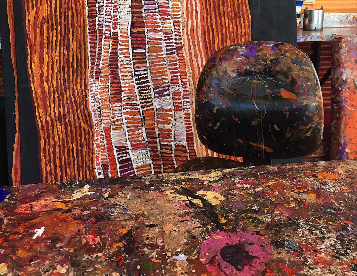 detail view of an Aboriginal artist's studio with paint on table and chair and painting behind.