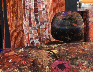 detail view of an Aboriginal artist's studio with paint on table and chair and painting behind.