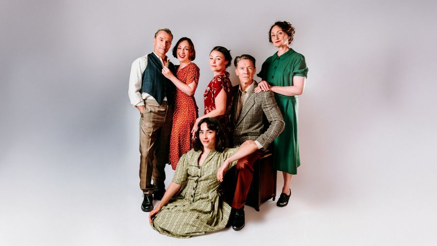 The cast of Red Stitch's 2026 centrepiece 'The Doll Trilogy'. The photo shows a group of six fair-skinned men and women, of varying ages, wearing costumes evoking the 1940s and 50s.