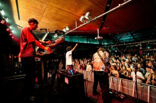 Northeast Party House play the UOW Uni Bar as part of Great Southern Nights 2025. The photograph , taken from the side of the stage, shows the alt-electro dance band's members playing live with a university student crowd dancing and enjoying the gig visible in front of the stage. The photograph illustrates a story on AI copyright advocacy.