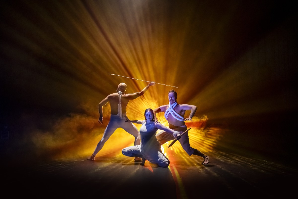 Joel Bray Dance's 'Garabari' features in the Blak Out program at Sydney Festival 2026.. Three First Nations people, two male-presenting and one female-presenting, pose dramatically on a smoky, yellow-lit back-lit stage. Sydney Festival 2026.