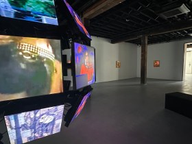 Gallery view of a video installation of televisions screens in an orb and paintings in background. AI art
