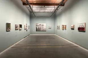 Gallery setting with paintings of various shapes all still lives on soft blue walls. Mirra Whale