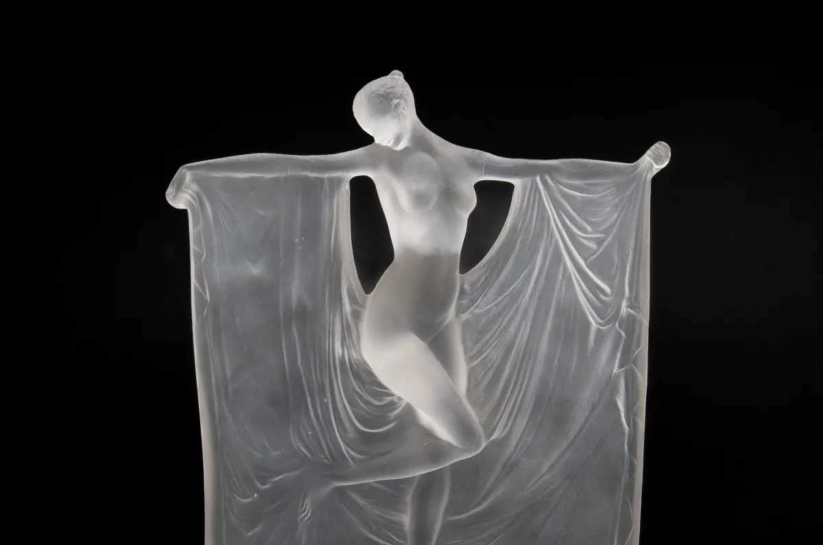 Glass sculpture of woman with outstretched arts and draped fabric in Art Deco style.