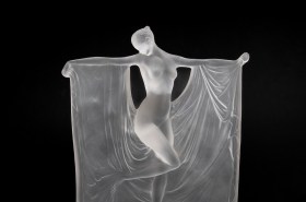 Glass sculpture of woman with outstretched arts and draped fabric in Art Deco style.