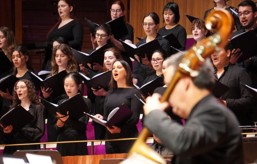 Sydney Philharmonia Choirs' 'A Child of Our Time'. A diverse group of singing choristers dressed in black and holding songbooks; an out of focus musician playing a double bass is pictured in the foreground.