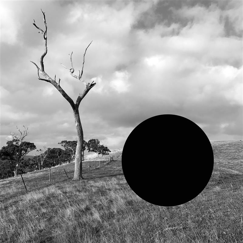 A black and white photograph of a rural Australlian landscape, showing a paddock, wire fence and trees; a stark black circle is superimposed or removed from the right hand side of the photo. AGSA 2026