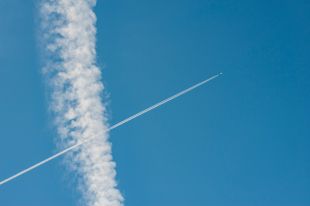 A passenger jet's contrail draws a diagonal line across a blue sky, intersecting with a puffy cloud that runs vertically from the top to the bottom of the frame. arts sector appointments