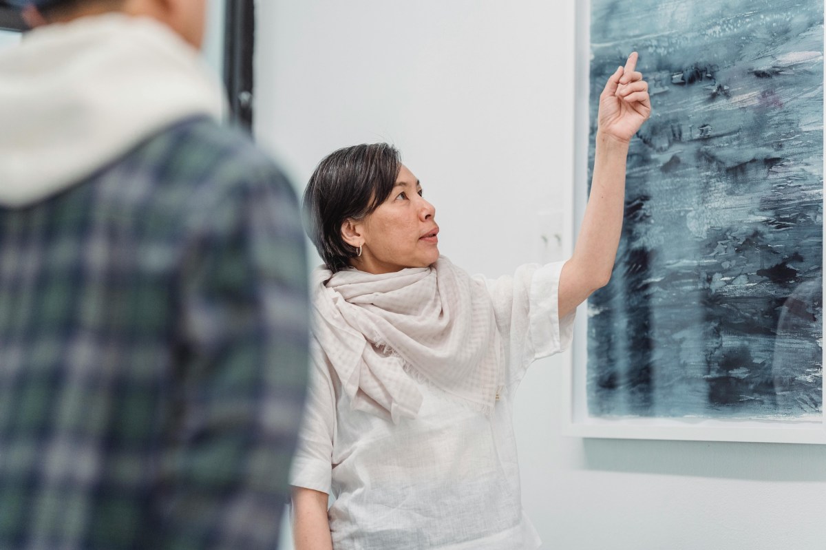 female asian artist talking about her painting in a gallery setting. museum