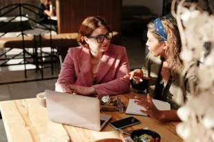 Two women at a desk in conversation in a creative business setting.