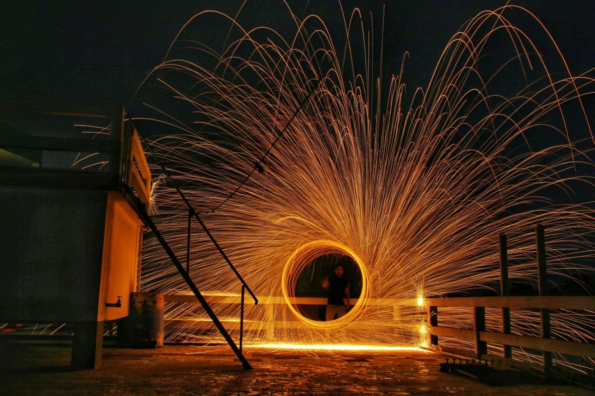 A person draws circles of light in the air with a firework; they are faintly visible at its centre, surrounded by circles of light and dramatically flying sparks.