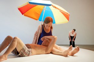 Hyperreal sculpture in gallery setting of man and woman at beach. Ron Mueck