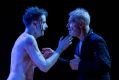 L-R: Tom Conroy and Colin Friels in Belvoir's 2025 production, 'The True History of the Life and Death of King Lear and his Three Daughters'. A bloodied, pale and shirtless younger man and an older, grey-haired man, speak intently to one another in a moody photograph of Belvoir's Shakespeare production.