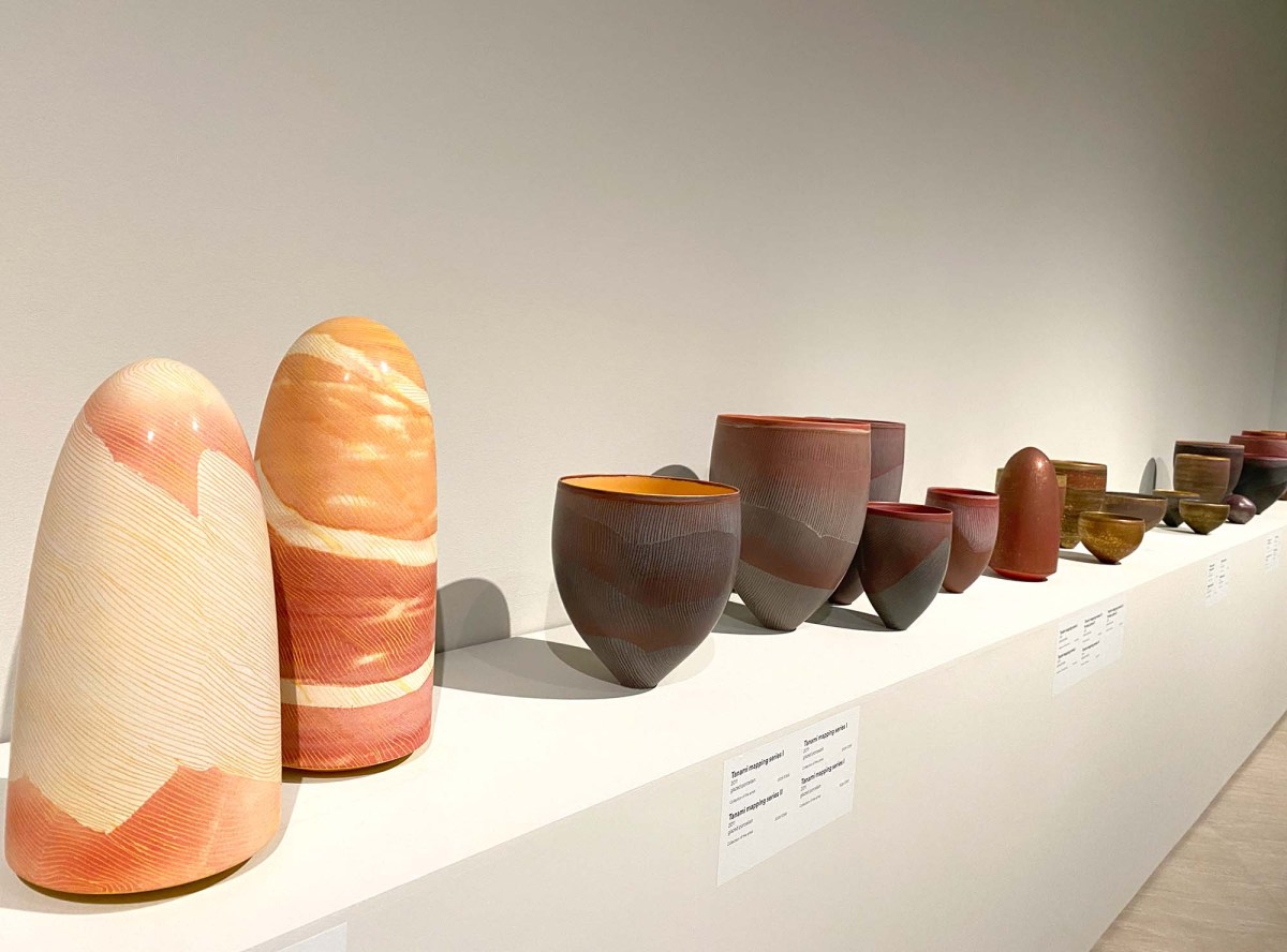 Pippin Drysdale: Infinite Terrain Major Retrospective exhibition 2025: a photo of red-orange ochre coloured large ceramic vessels and stone like forms displayed on a white shelf against a white wall in a contemporary gallery space.