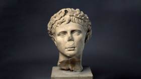 Image of a musem sculpture of a stone head with a missing nose. Roman Empire