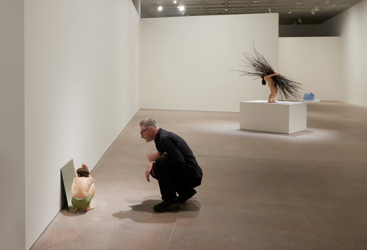 Man looking at hyperreal sculpture in gallery setting. Ron Mueck