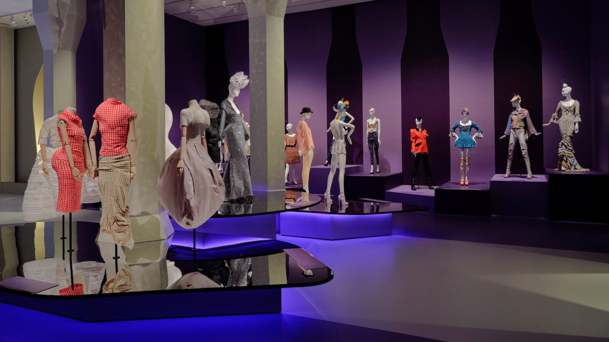 Busy exhibition display of fashion with purple lights. Westwood / Kawakubo