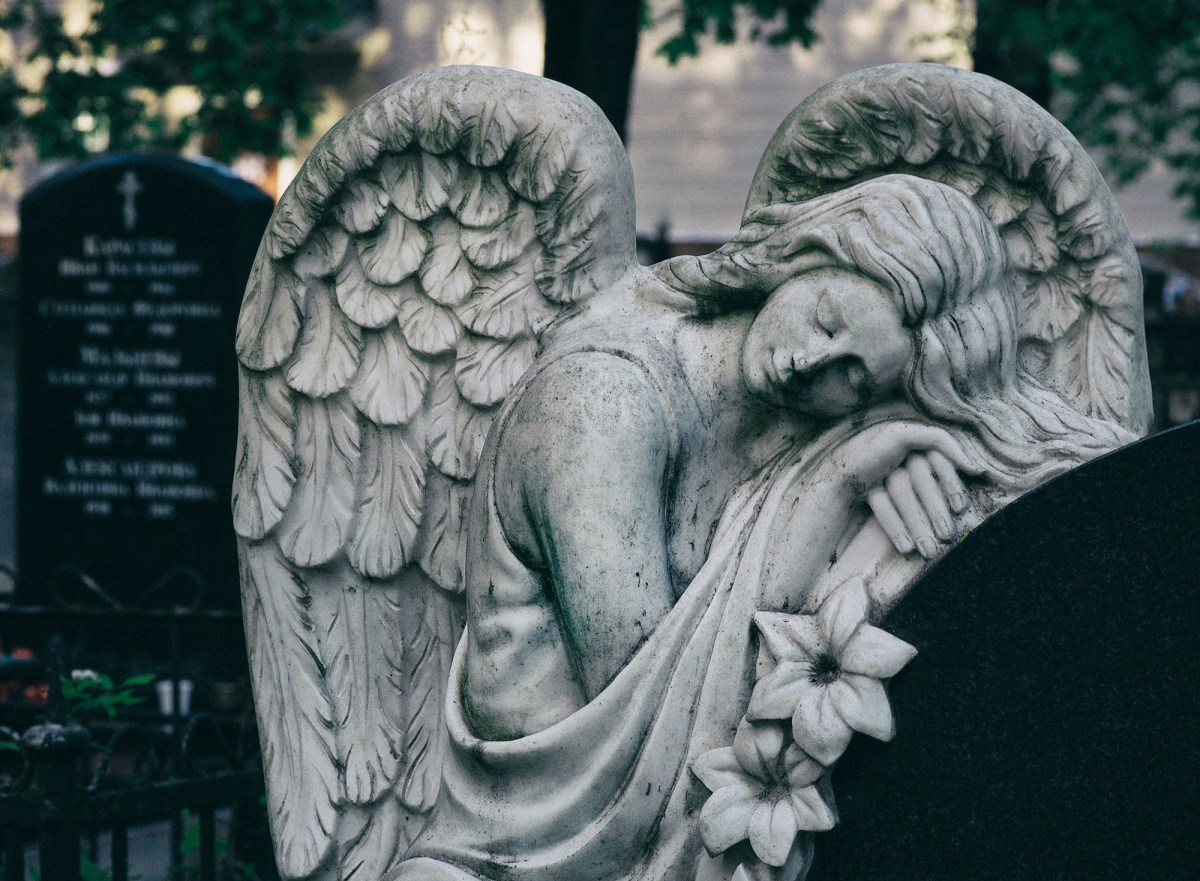 Black and white photo of an angel leaning on a tombstone. Vale 2025.