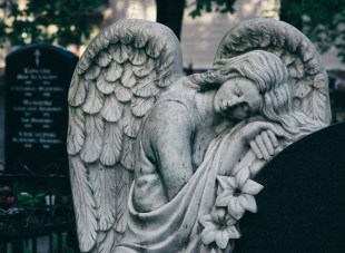 Black and white photo of an angel leaning on a tombstone. Vale 2025.