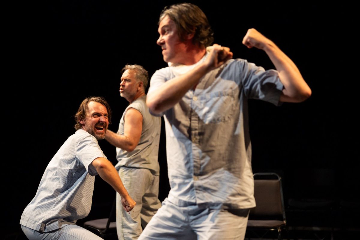 A scene from Hamlet Camp, now playing at Carriageworks. Three fair-skinned, middle aged men dressed in white, are photographed in the midst of an intense performance.