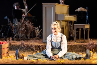 Kala Gare in MTC's 2026 production of My Brilliant Career. Gare sits on stage in period dress as her character, Sybylla Melvyn; she grins devilishly and sits with her legs spread wide.