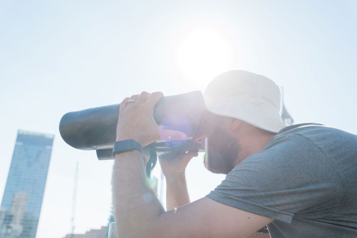 Julia Phillips' Observer, Observed at Sydney Festival 2026. A man ion a white Terry Towling hat peers through a pair of bespoke binoculars, which form part of the artwork.