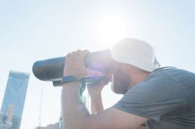 Julia Phillips' Observer, Observed at Sydney Festival 2026. A man ion a white Terry Towling hat peers through a pair of bespoke binoculars, which form part of the artwork.