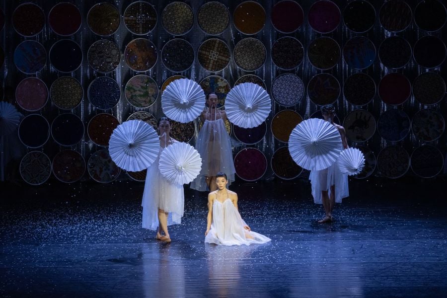 Post-Orientalist Express, 2026. Three dancers dressed in white hold white paper umbrellas towards the audience; a fourth dancer, also in white, kneels between them.