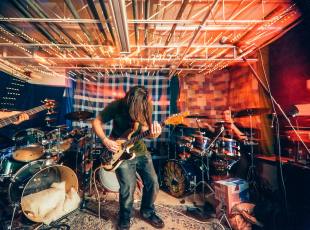 A rock band rehearses in a home-made garage studio, complete with blankets over the windows to help muffle the noise. Grants and opportunities for musicians in 2026