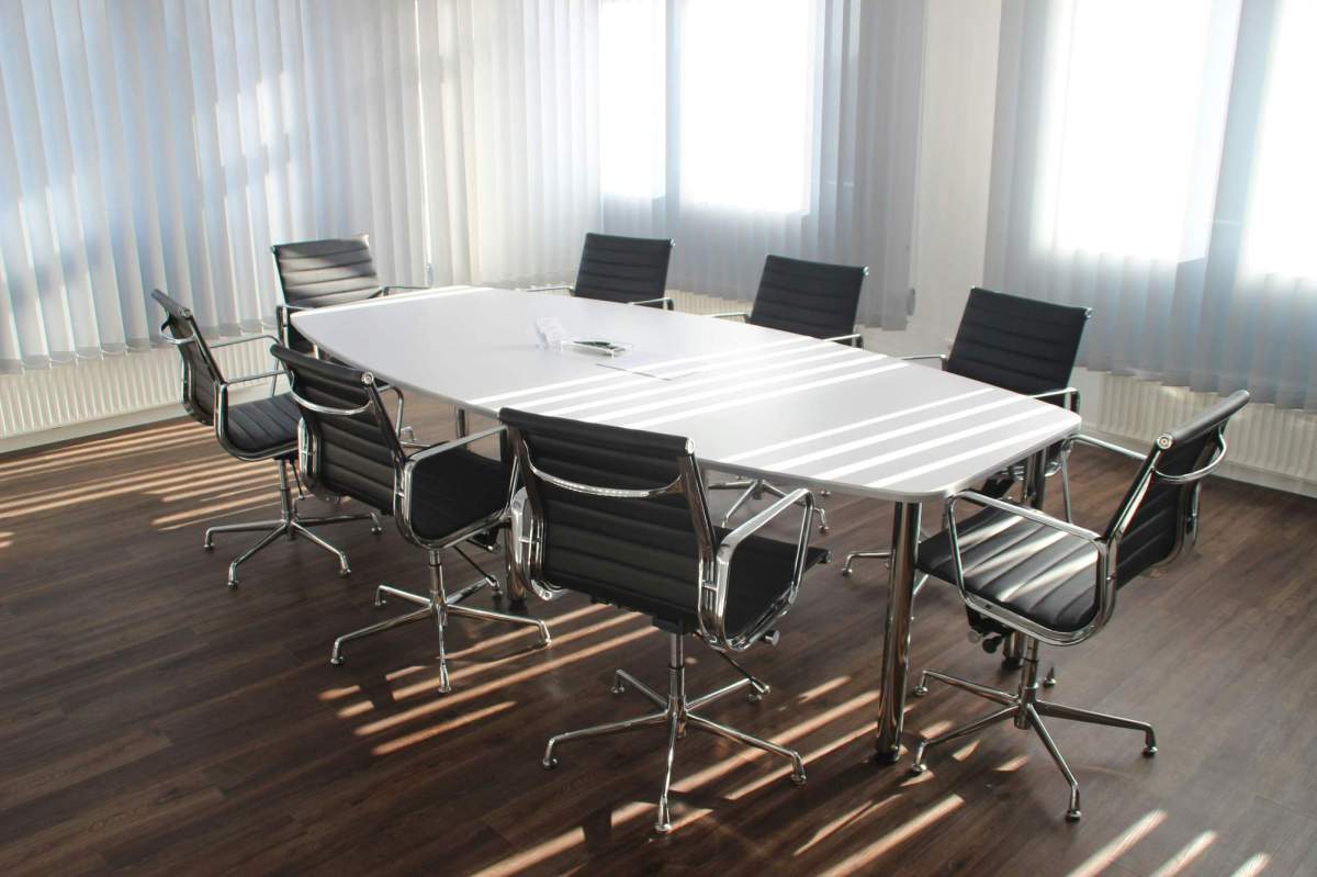 arts board in crisis: a photo of a room with an empty board room table. It's a white oblong table with 8 executive style black chairs around it.