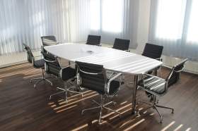 arts board in crisis: a photo of a room with an empty board room table. It's a white oblong table with 8 executive style black chairs around it.