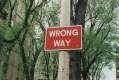 arts governance: photo of a red and white street sign that says "wrong way" against a background of trees in the street.