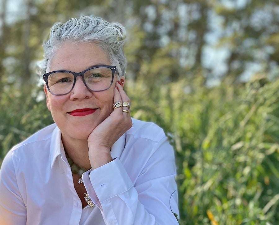 Gina Fairley. A stylish, middle-aged woman with short grey hair and glasses. She sits with her chin in her left hand and smiles warmly at the camera.